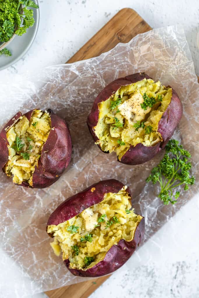 An overview shot of a baked sweet potato topped with butter and parsley