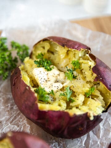 An overview shot of a baked sweet potato topped with butter and parsley