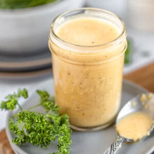 An overview shot of a jar of apple cider vinegar dressing in a jar next to a spoon and parsley on top of grey plates