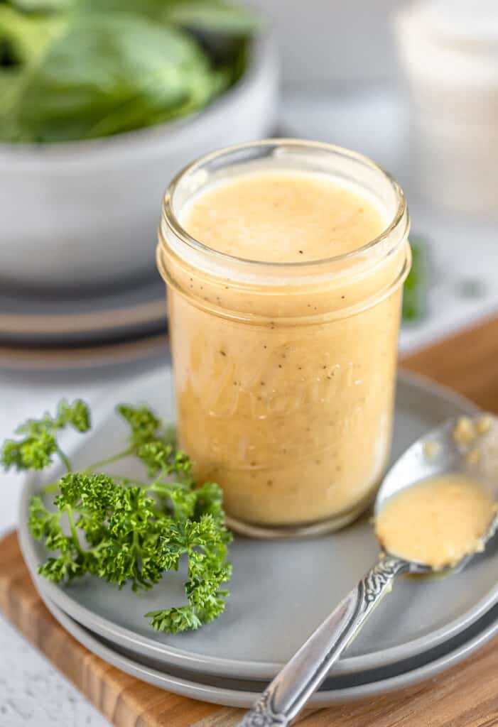 An overview shot of a jar of apple cider vinegar dressing in a jar next to a spoon and parsley on top of grey plates