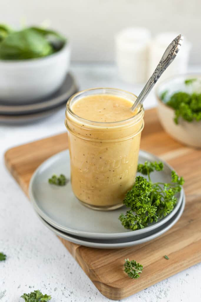 An overview shot of a jar of apple cider vinegar dressing in a jar next to a spoon and parsley on top of grey plates