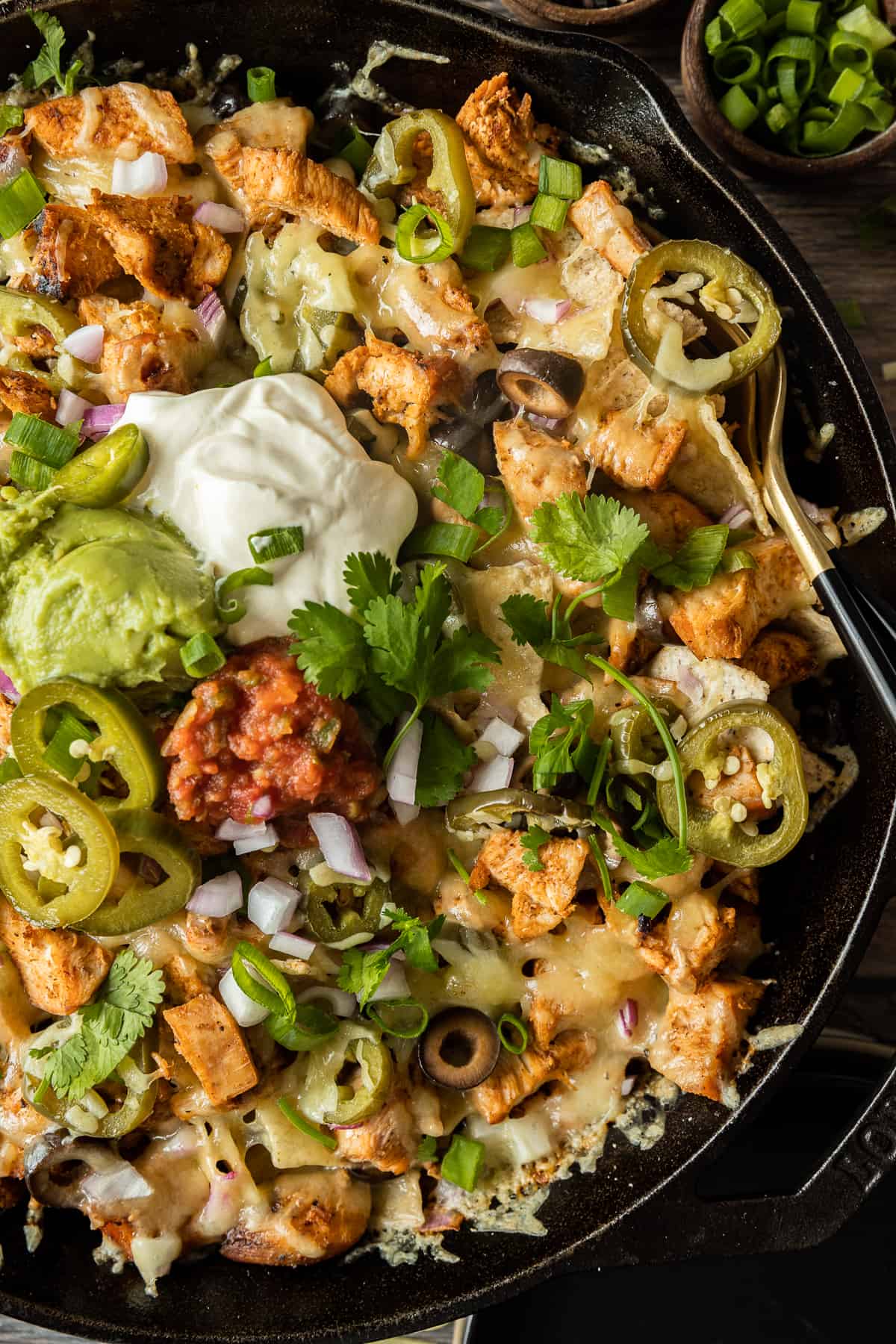 An overview shot of a cast iron skillet filled with nachos and topped with sour cream, guacamole, cilantro, and salsa.