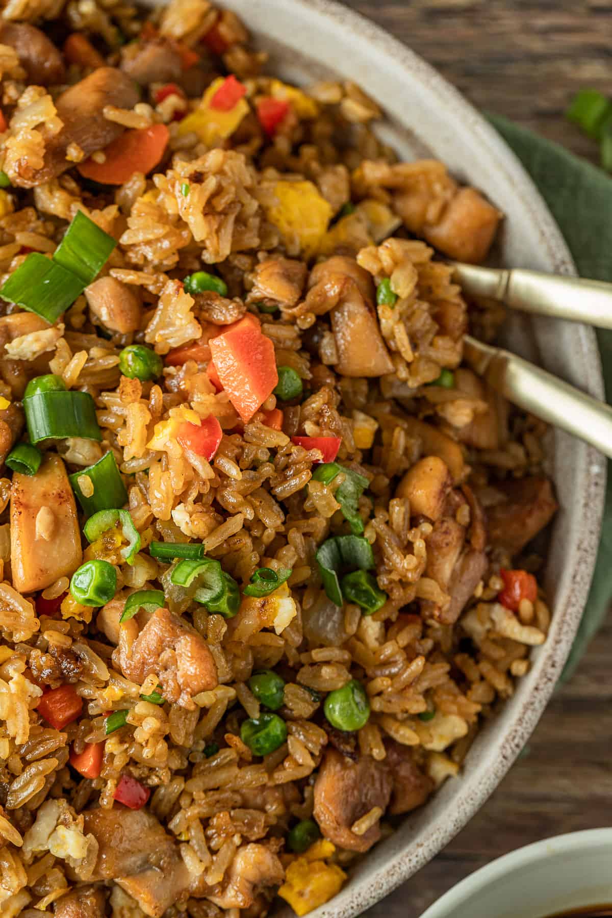 An overview shot of a bowl of chicken fried rice in a bowl with two gold spoons.