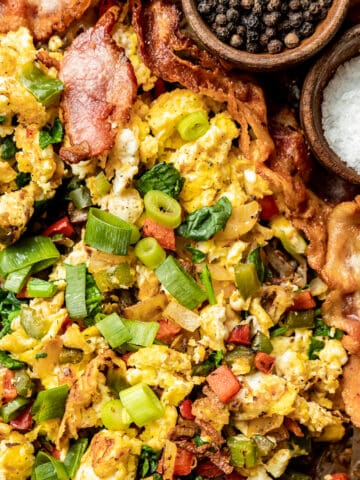 An overview shot of eggs, hashbrowns, and bacon on a baking sheet topped with green onions, salt, and pepper.