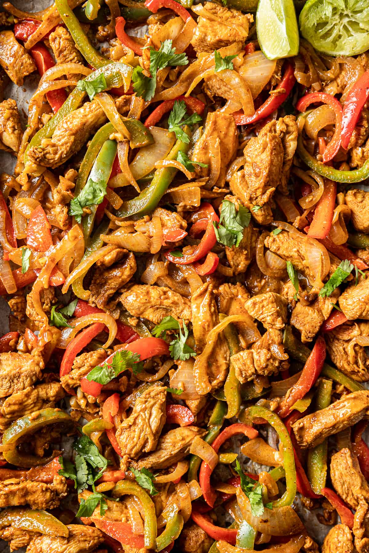 An overhead closeup shot of chicken fajitas on a pan topped with chopped cilantro and lime wedges.