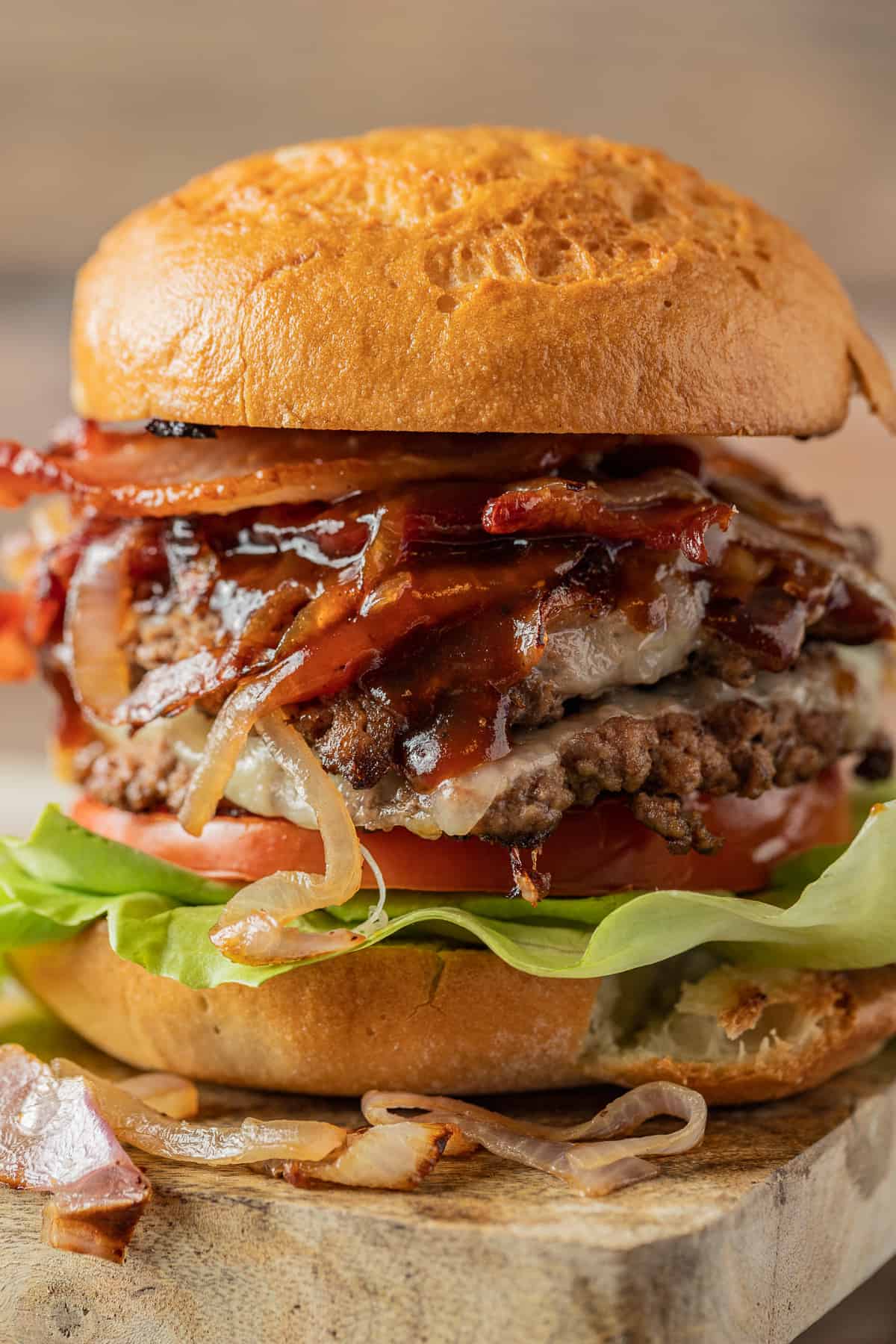 Two smash burger patties between a hamburger bun topped with lettuce, tomato, bbq sauce, and onions.