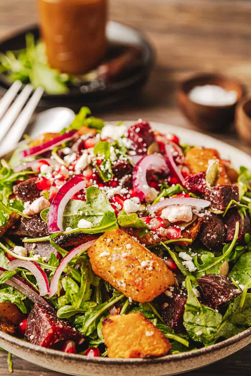 A close up shot of a roasted butternut and beetrood salad in a cream bowl on a wood background