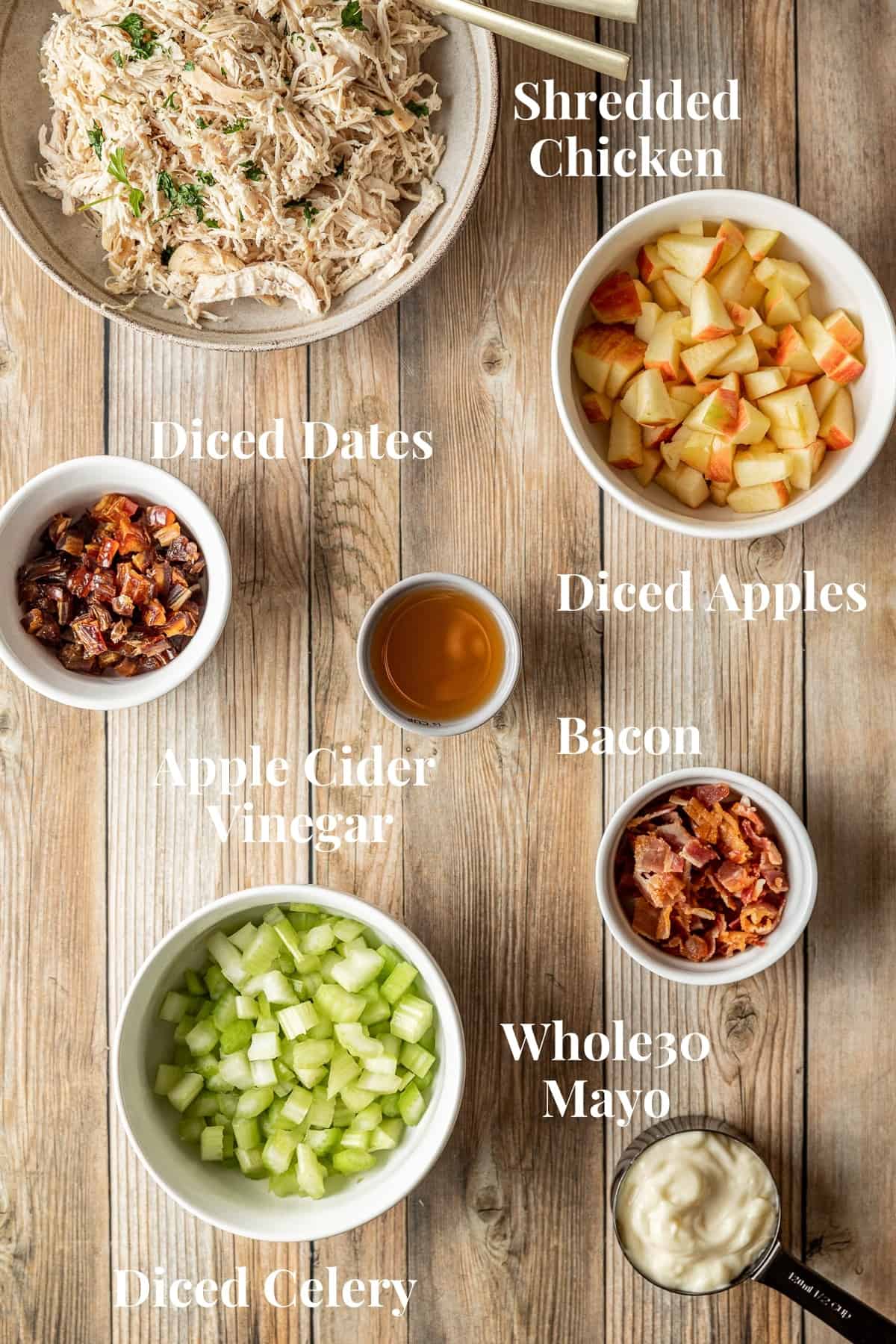 Verious sized bowls containing chicken salad ingredients on a wood background.