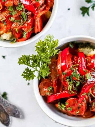 Two bowls of coconut curry with peppers and onion next to two spoons and parsley