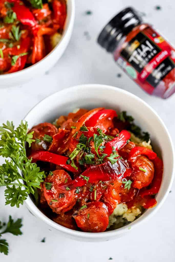 Two bowls of thai coconut curry next to a jar of red curry paste