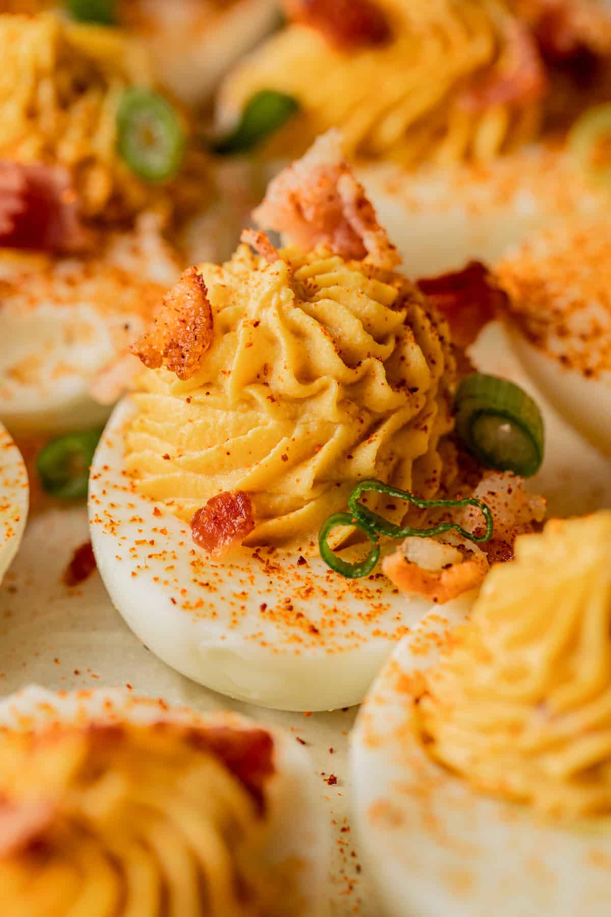 A close up shot of a deviled egg topped with bacon and smoked paprika.