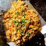 An overview shot of chicken fried rice on a blackstone griddle being tossed by two spatulas.