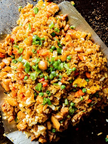 An overview shot of chicken fried rice on a blackstone griddle being tossed by two spatulas.