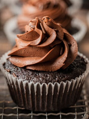 A close up photo of a chocolate cupcake with chocolate buttercream swirl on a wire cooling rack.