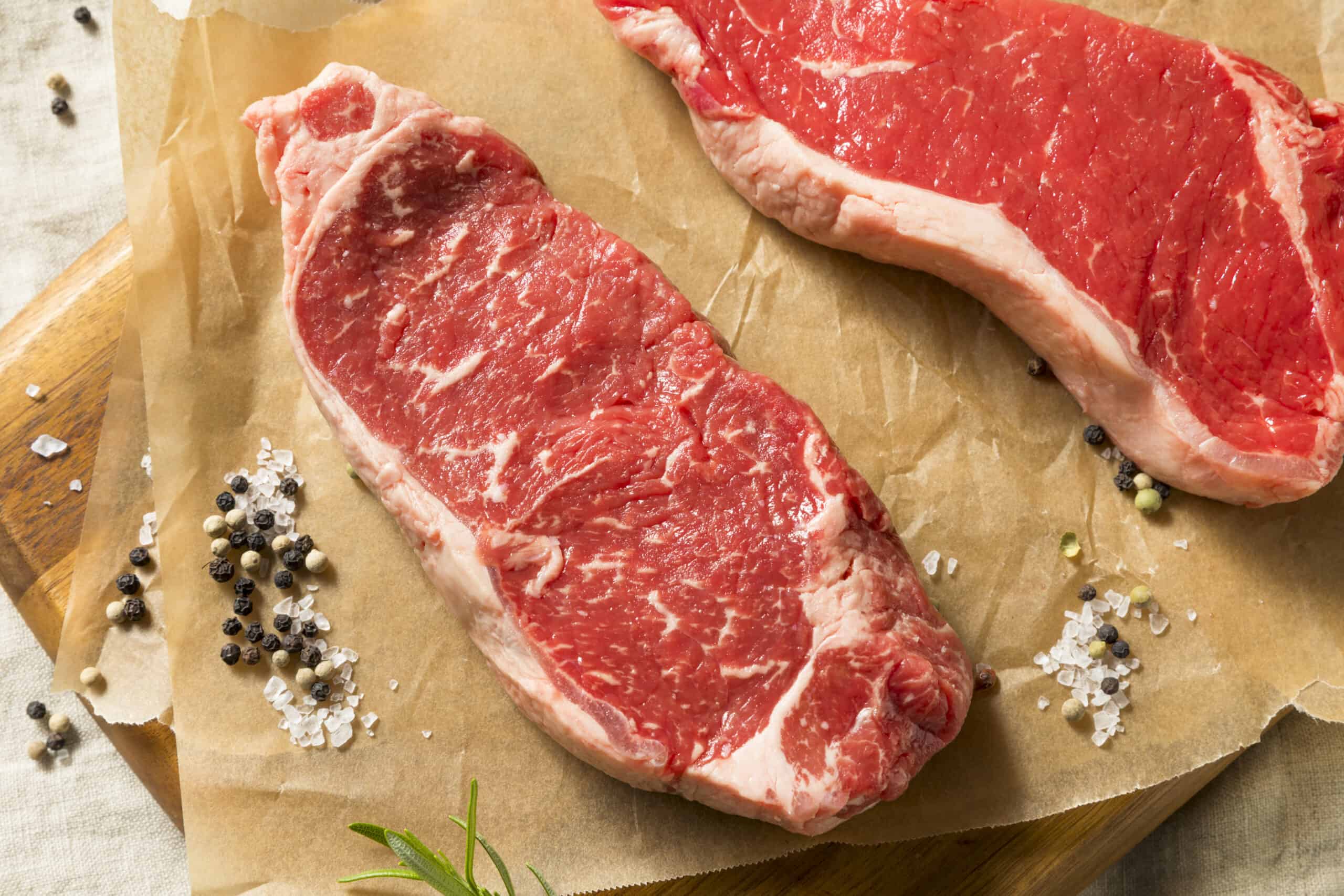 Raw Grass Fed NY Strip Steaks with Salt and Pepper on butcherpaper