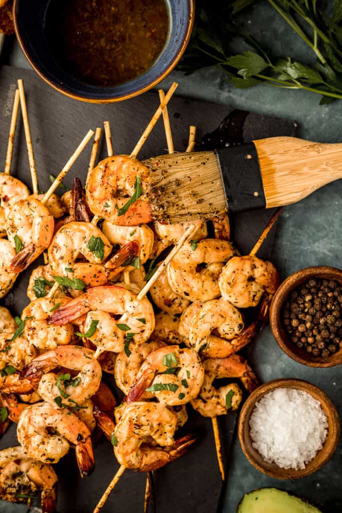 An overhead shot of smoked shrimp skewers on a black serving board next to Whole30 marinade and garnishes