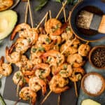 An overhead shot of smoked shrimp skewers on a black serving board next to Whole30 marinade and garnishes