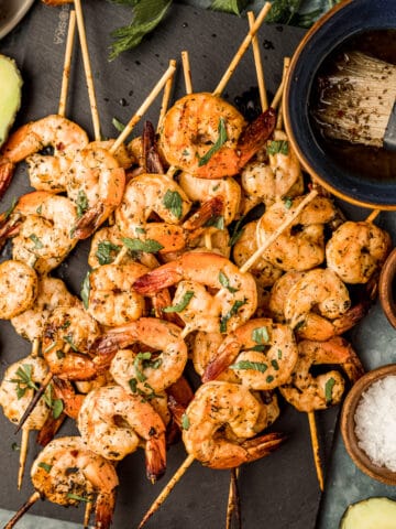 An overhead shot of smoked shrimp skewers on a black serving board next to Whole30 marinade and garnishes