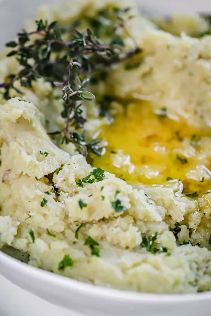 Instant pot mashed sweet potatoes in a white bowl topped with herbs and melted ghee