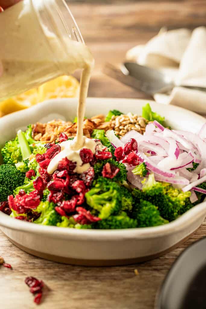 Paleo dressing being poured over broccoli and bacon salad on a wood background