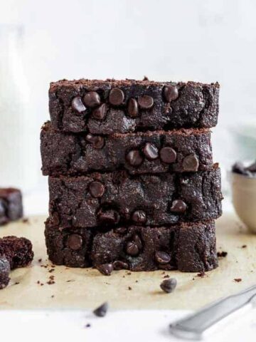 A stack of double chocolate chip banana bread next to a bowl of chocolate chips and a glass of milk