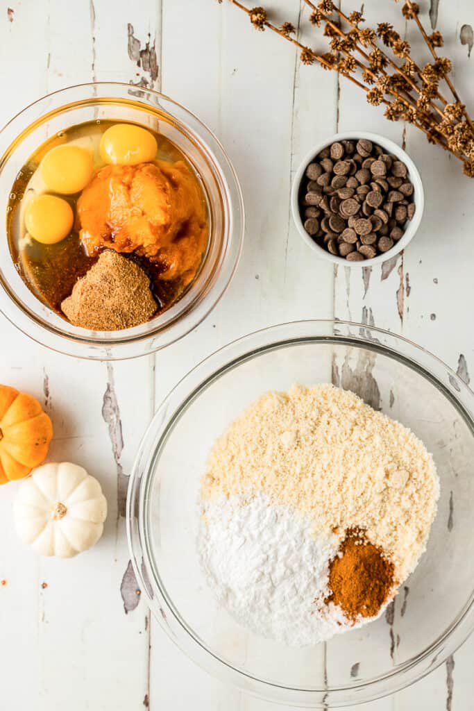 An overview shot of two bowls containing wet and dry ingredients for paleo pumpkin and chocolate chip muffins