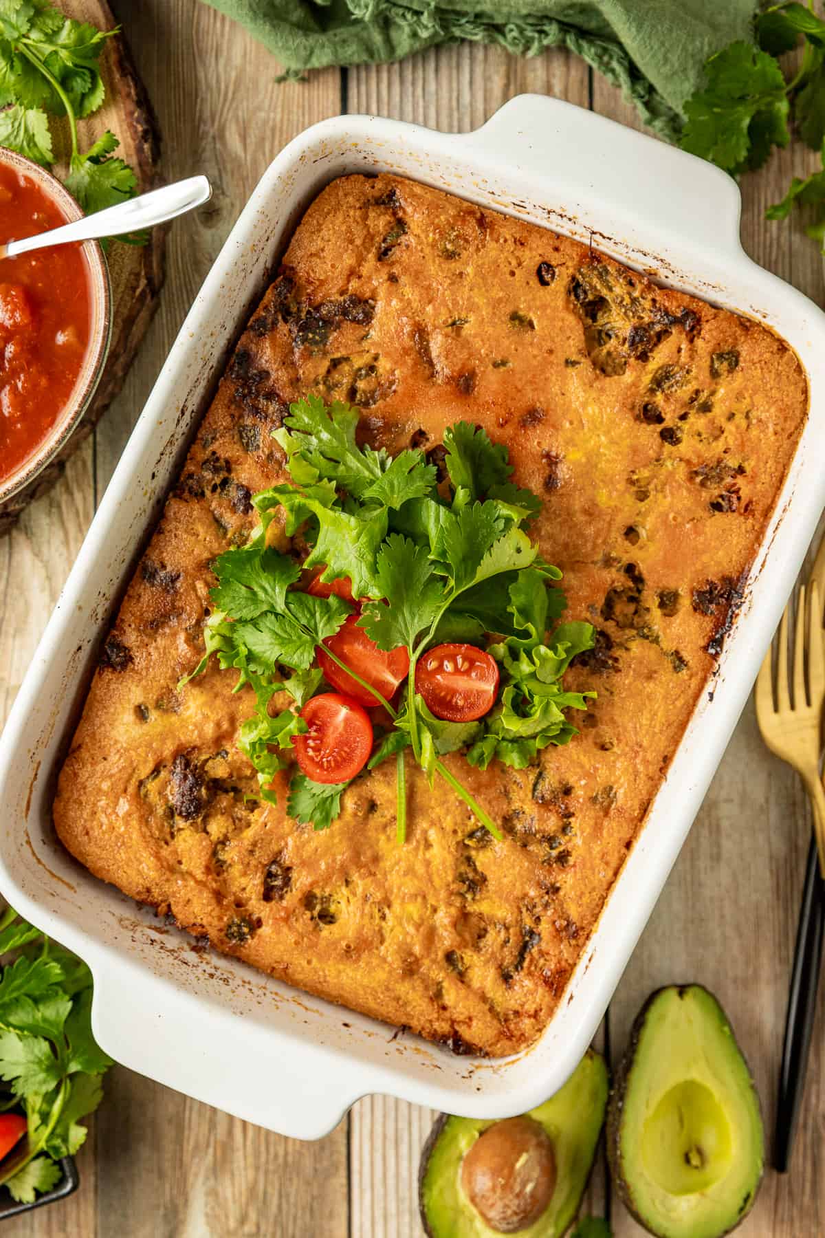 An overview shot of a paleo taco casserole in a white casserole dish topped with cilantro, tomatoes, and lettuce on a wood background.