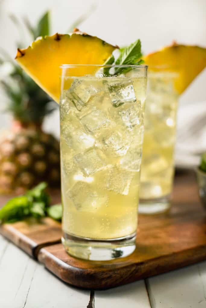 Two pineapple mojito mocktails on a cutting board topped with pineapple and mint