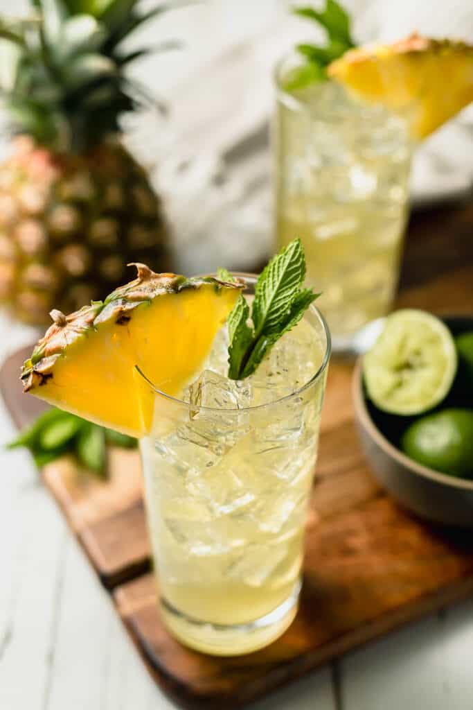 Two pineapple mojito mocktails on a cutting board topped with pineapple and mint