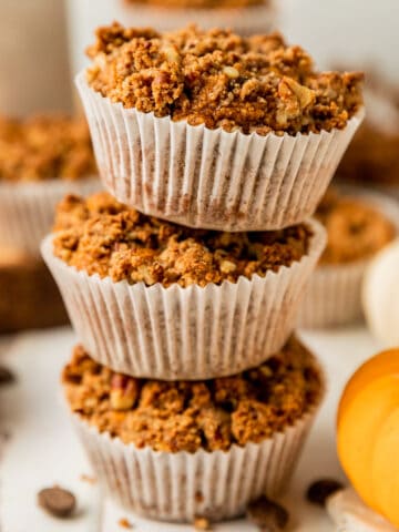 A stack of paleo pumpkin chocolate chip muffins on a white wood background near cinnamon sticks and chocolate chips