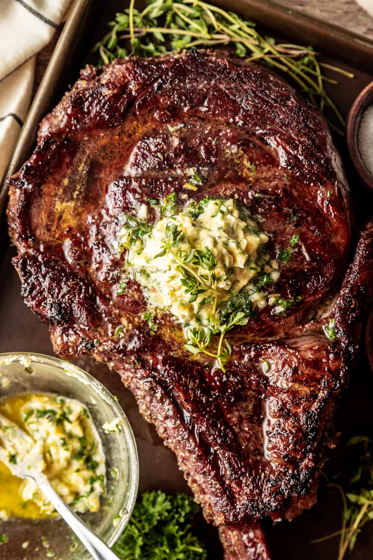 An overview shot of a juice reverse seared tomahawk steak on a baking sheet topped with a herb butter compound.