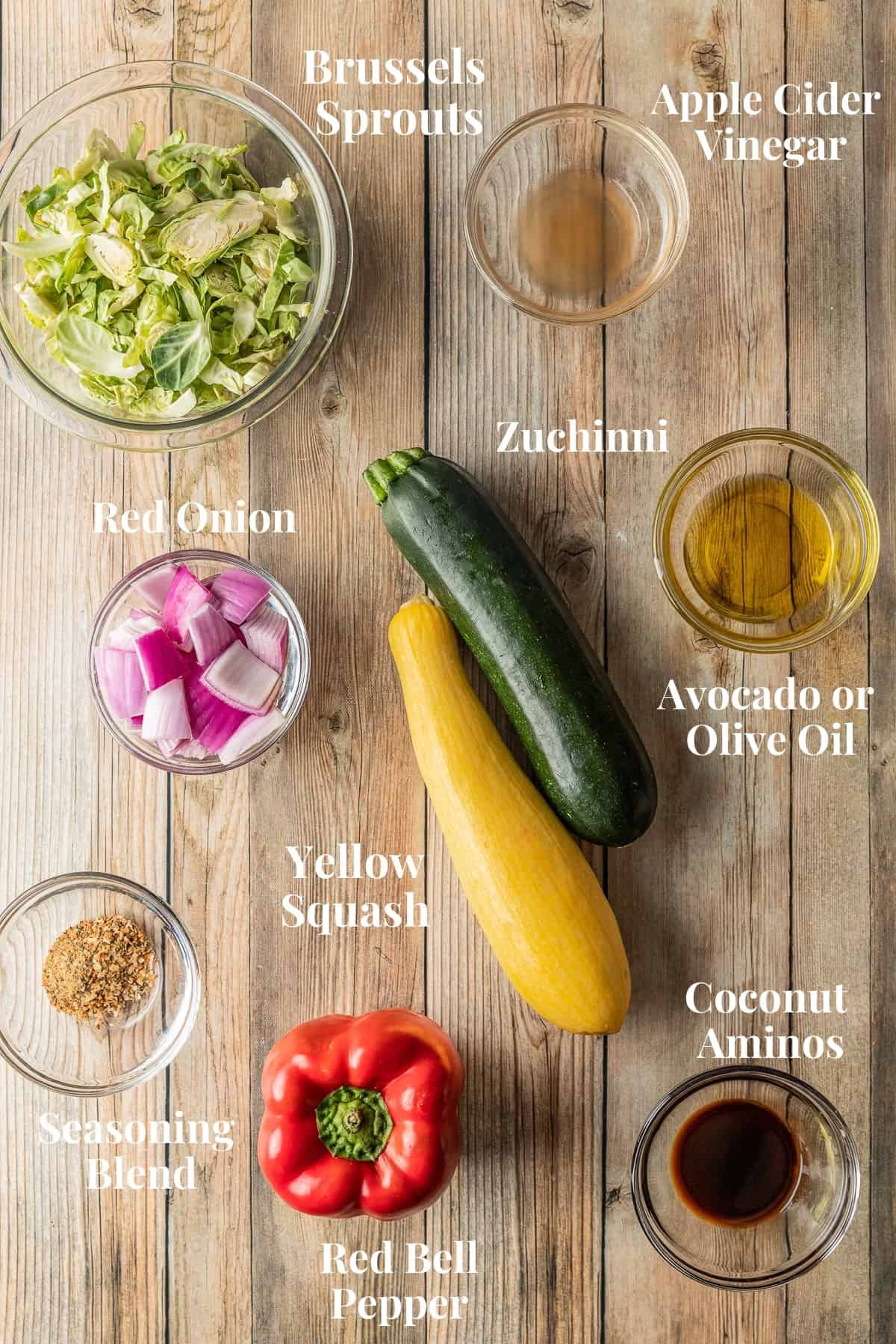 An overview shot of the ingredients needed for smoked vegetables in glass bowls on a wood background.