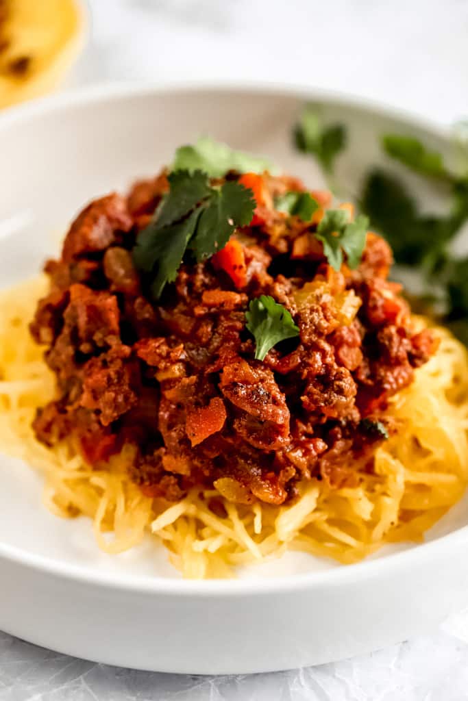 A white bowl of spaghetti squash topped with spaghetti meat sauce 