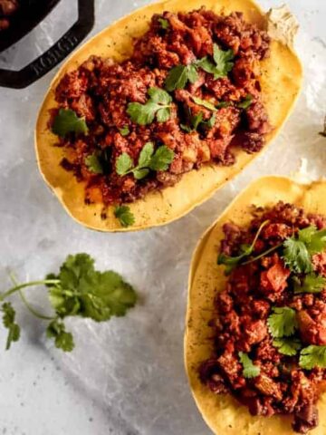 Two spaghetti squash halves filled with spaghetti meat sauce topped with parsley on a grey background