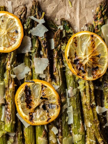 An overview shot of grilled asparagus spears topped with grilled lemon, parmesean cheese, and cracked black pepper.