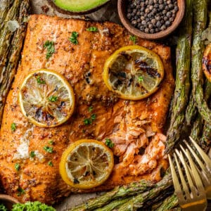 An overview shot of a whole salmon fillet topped with lemon and served with roasted asparagus.