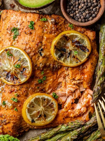 An overview shot of a whole salmon fillet topped with lemon and served with roasted asparagus.