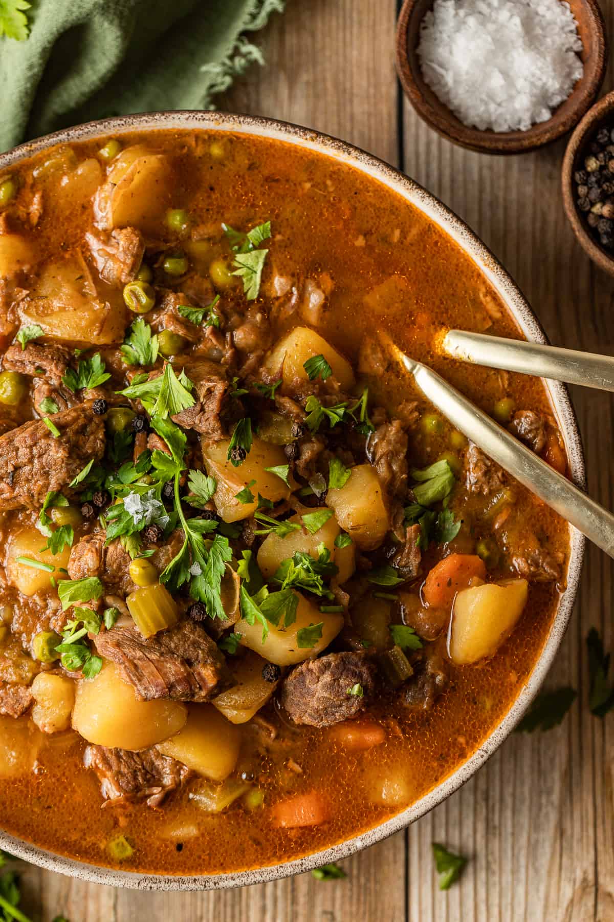 An overview shot of a bowl of beef stew on a wood background near a green linen.