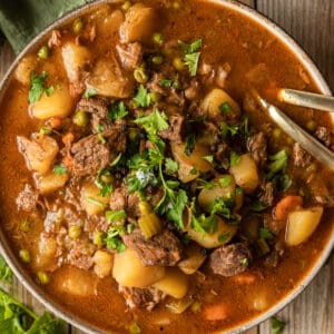 An overview shot of a bowl of beef stew on a wood background near a green linen.