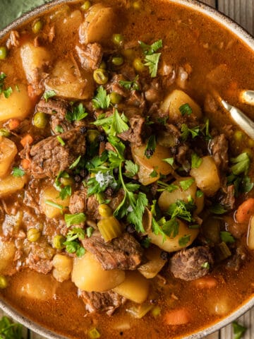 An overview shot of a bowl of beef stew on a wood background near a green linen.