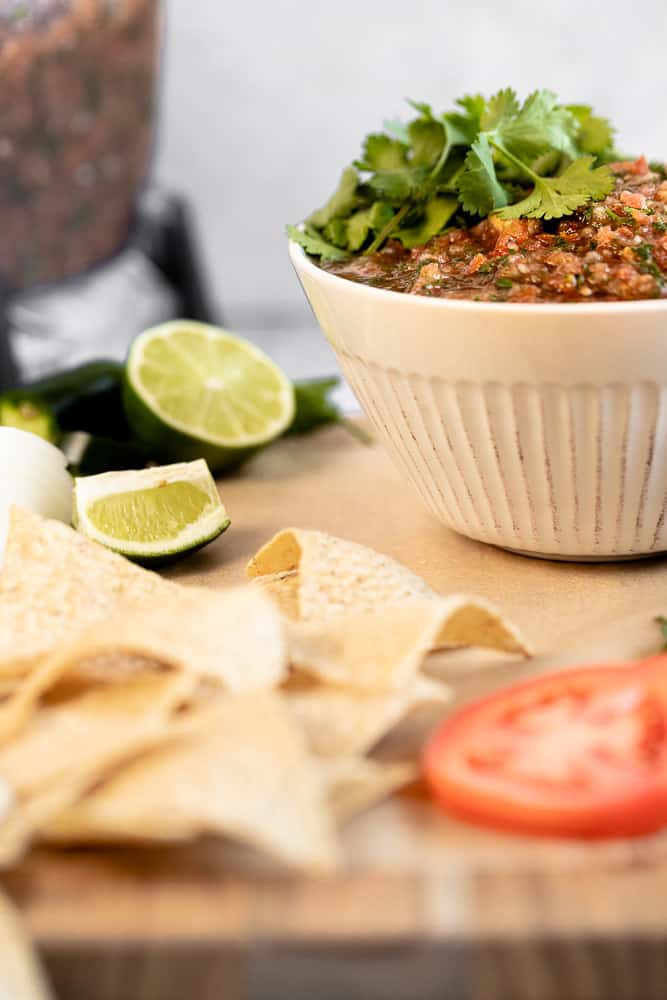 A bowl of Whole30 salsa on a cutting board next to a blender