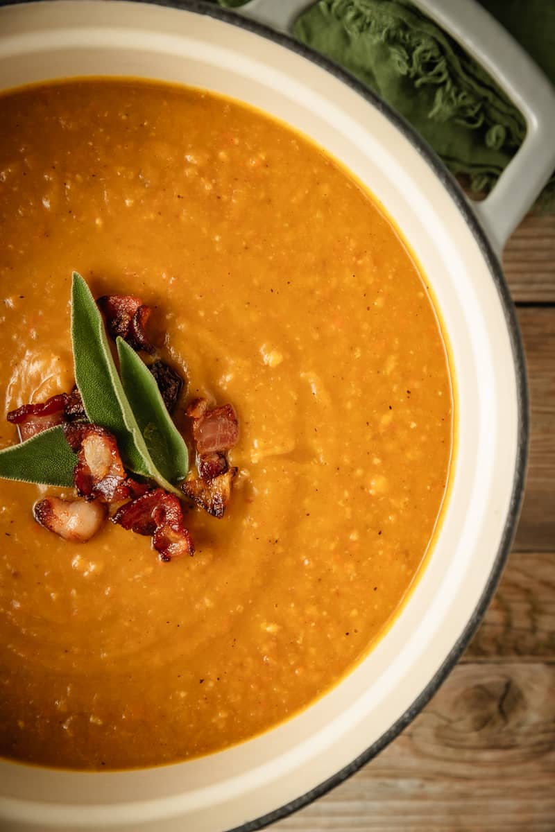 An overhead shot of creamy dairy free butternut squash soup in a dutch oven on a wood background near a green linen.