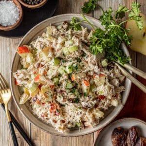 Chicken salad in a bowl on a wood background near dishes of salt, pepper, and dates.