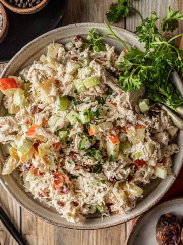 Chicken salad in a bowl on a wood background near dishes of salt, pepper, and dates.