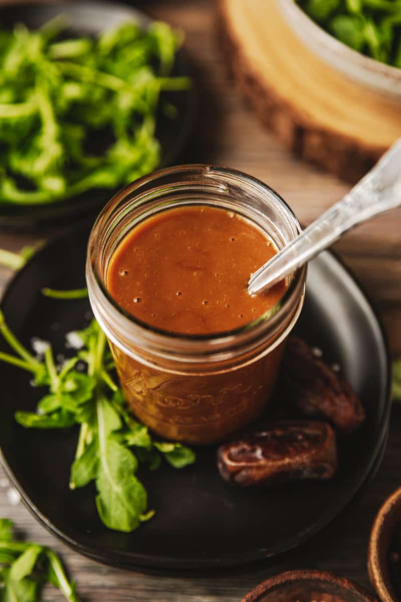 A mason jar of Whole30 date and dijon dressing on a black plate near greens