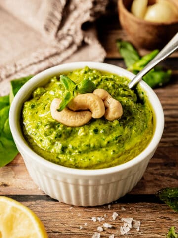 A bowl of whole30 pesto topped with cashews and olive oil on a wood background