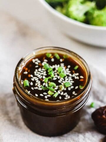 A jar of whole30 teriyaki sauce next to a bowl of broccoli and dates